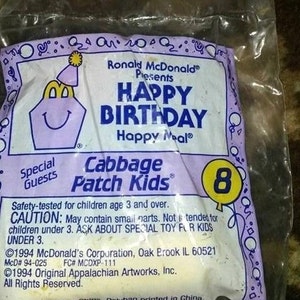 May include: Sealed Happy Meal toy bag featuring Ronald McDonald and Cabbage Patch Kids branding. The bag is purple and white, with "Happy Birthday" text and a number 8 balloon graphic. Safety information is also printed on the bag.