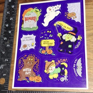 May include: Sheet of Halloween-themed stickers with various spooky illustrations on a purple background. Designs include a ghost, witch, spider, pumpkins, and phrases like "Beware!" and "Watch Out!" The stickers are in a variety of colors.