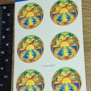Puede incluir: Hoja de pegatinas autoadhesivas con un diseño de puesta de sol en el océano. Cada pegatina muestra un sol amarillo que se pone sobre agua azul, palmeras y una playa de arena. El texto "OCEAN SUNSET" está impreso en la hoja. La marca es "ILLUMINATIONS".