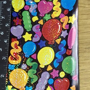 Puede incluir: Hoja de pegatinas de fiesta coloridas con globos, estrellas y serpentinas. Las pegatinas son de varios colores, incluyendo amarillo, azul, rojo y morado, con acentos de purpurina. El texto "©2001 Sandylion Sticker Designs" es visible.