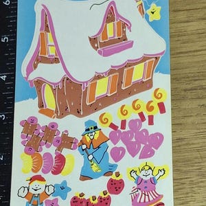 Puede incluir: Una hoja de pegatinas vintage con el texto "Decorate a Witch's House". La hoja presenta una casa de jengibre, hombrecitos de jengibre, una bruja, corazones, piruletas y otras ilustraciones caprichosas en colores brillantes.