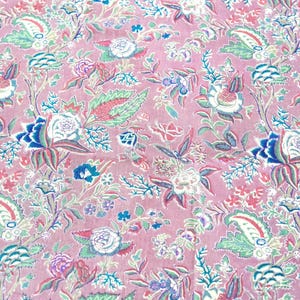 May include: A fabric featuring a repeating floral pattern on a dusty pink background. The design includes stylized flowers, leaves, and paisley-like shapes in shades of white, dark blue, light blue, and green, creating a dense, intricate botanical print.