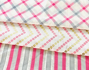 May include: Three fabric swatches with different patterns. The top swatch has a white background with a pink and gray plaid design. The middle swatch has a white background with a repeating pattern of pink and gold squares. The bottom swatch has pink and gray vertical stripes.