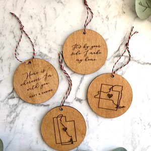 Puede incluir: Tres adornos de madera con colgadores de cuerda. Un adorno presenta el texto "Home is wherever I'm with you. MATT & SABINA". Otro adorno presenta el texto "It's by your side I make my home." El tercer adorno presenta un coraz&oacute;n dentro del contorno de un estado.
