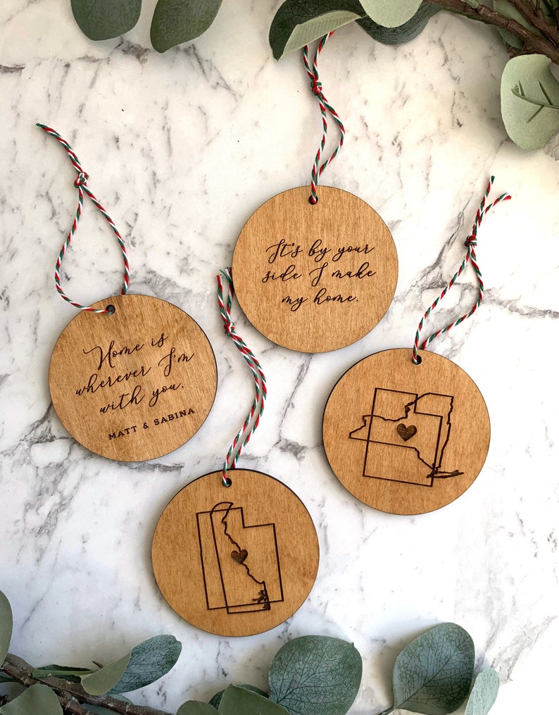 Puede incluir: Tres adornos de madera con colgadores de cuerda. Un adorno presenta el texto "Home is wherever I'm with you. MATT & SABINA". Otro adorno presenta el texto "It's by your side I make my home." El tercer adorno presenta un coraz&oacute;n dentro del contorno de un estado.