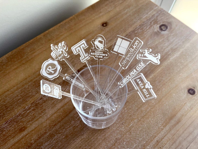 Custom acrylic drink stirrers with engraved corporate logos, displayed in cocktail glasses at a networking event.