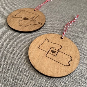 Puede incluir: Dos adornos de madera con forma de los estados de Pensilvania y Ohio con un coraz&oacute;n en el medio de Ohio. Los adornos cuelgan de un cordel rojo y blanco.