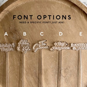K&ouml;nnte beinhalten: F&uuml;nf verschiedene Schriftarten f&uuml;r personalisierte Acryl-R&uuml;hrst&auml;bchen. Die Optionen sind mit A bis E gekennzeichnet. Option A lautet "Jordan & Austin", Option B lautet "Abby & Kyle", Option C lautet "The Glenns", Option D lautet "+ the cannons +" und Option E lautet "Danielle & Jason".