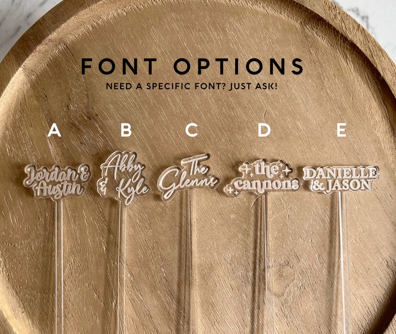 K&ouml;nnte beinhalten: F&uuml;nf verschiedene Schriftarten f&uuml;r personalisierte Acryl-R&uuml;hrst&auml;bchen. Die Optionen sind mit A bis E gekennzeichnet. Option A lautet "Jordan & Austin", Option B lautet "Abby & Kyle", Option C lautet "The Glenns", Option D lautet "+ the cannons +" und Option E lautet "Danielle & Jason".