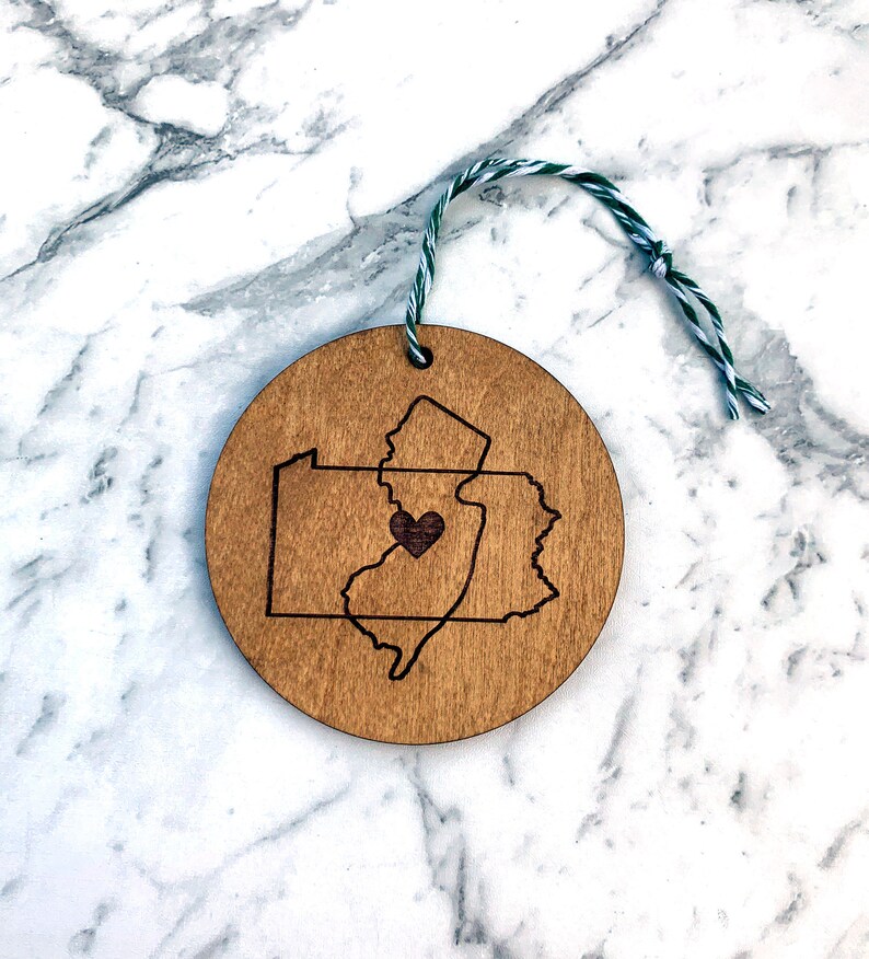 Puede incluir: Un adorno de madera con forma de los estados de Nueva Jersey y Pensilvania, con un coraz&oacute;n en el centro de Nueva Jersey.
