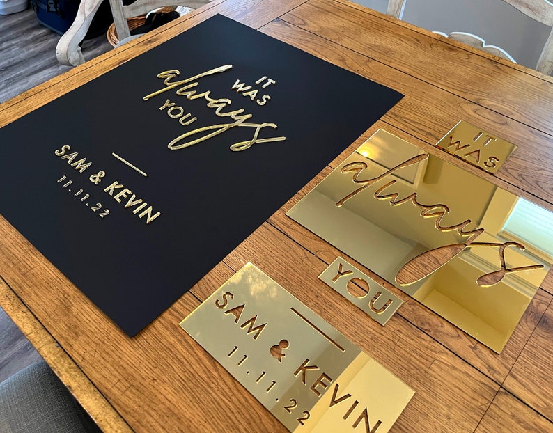 K&ouml;nnte beinhalten: Ein schwarzes Schild mit goldfarbenen Buchstaben, auf dem "It was always you" und die Namen "Sam & Kevin" mit dem Datum "11.11.22" stehen. Goldene Spiegelausschnitte des gleichen Textes sind ebenfalls vorhanden.