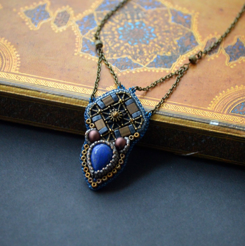 Puede incluir: Un collar de cuentas con un colgante geom&eacute;trico que presenta una piedra azul y detalles dorados.