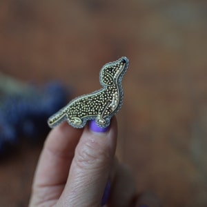 Puede incluir: Un broche de dachshund de cuentas en tonos marrones y dorados. El dachshund está de pie sobre sus patas traseras con la cabeza levantada.