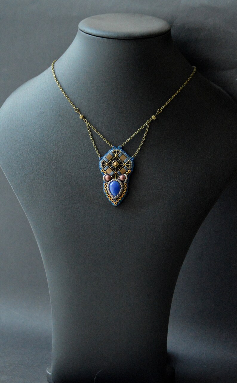 Puede incluir: Un collar de cuentas con un colgante geom&eacute;trico que presenta una piedra preciosa azul, detalles dorados y cuentas marrones.