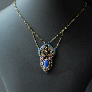 Puede incluir: Un collar de cuentas con un colgante geom&eacute;trico que presenta una piedra preciosa azul y detalles dorados.