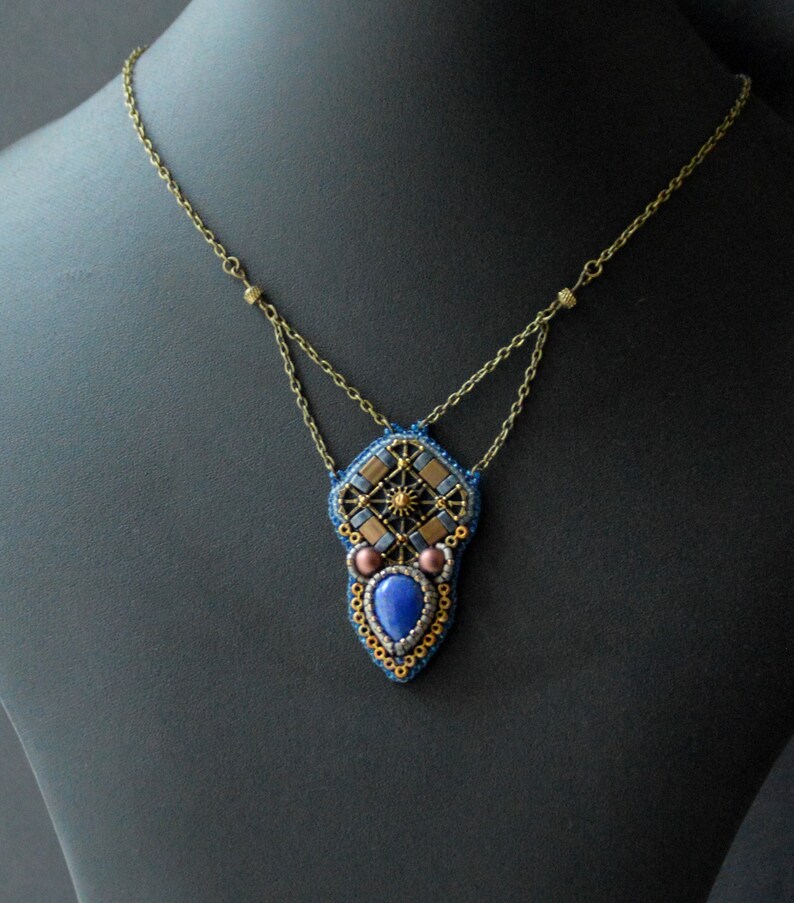 Puede incluir: Un collar de cuentas con un colgante geom&eacute;trico que presenta una piedra preciosa azul y detalles dorados.