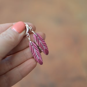 May include: A pair of silver hoop earrings with pink and white feather-shaped charms.