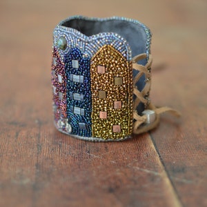 May include: A beaded bracelet with a multi-colored design of buildings. The bracelet is made of leather and has a lace-up closure.