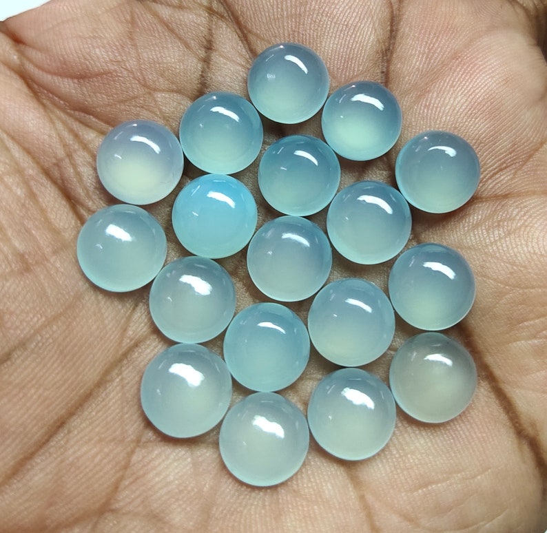 May include: A collection of 20 round, light blue, translucent cabochon gemstones. The stones are smooth and polished.