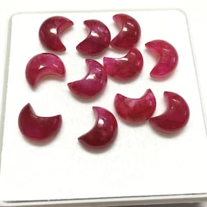 Peut inclure: Douze pierres précieuses en cabochon en forme de croissant de couleur rouge foncé. Les pierres précieuses sont disposées en un groupe lâche sur une surface blanche.