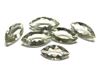 May include: A collection of six loose, marquise-cut gemstones with a pale, translucent green hue. Each stone features a faceted surface that reflects light, creating a clear, sparkling appearance with pointed ends and a symmetrical, elongated shape.
