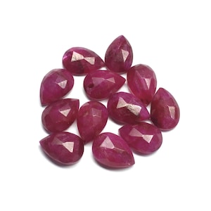 May include: A group of 13 faceted ruby gemstone drops in a pear shape. The stones are a deep pink color and have a glossy finish.