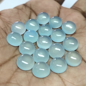 May include: A collection of 18 light blue cabochon gemstones, each with a smooth, rounded surface. The stones are arranged in a loose cluster on a hand.