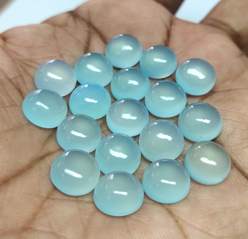 May include: A collection of 18 light blue cabochon gemstones, each with a smooth, rounded surface. The stones are arranged in a loose cluster on a hand.