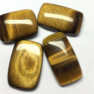 May include: Four polished tiger's eye stones, each with a rectangular shape and a golden brown color with dark brown stripes.
