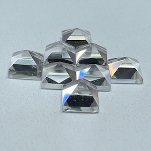 May include: A collection of seven clear, pyramid-shaped glass or crystal stones arranged in a cluster. Each piece features multiple faceted surfaces that reflect light, creating subtle prismatic colour shifts across the transparent, geometric forms.