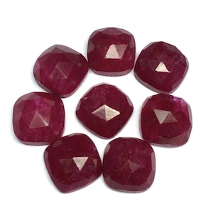 Puede incluir: Ocho gemas facetadas, de talla cojín, de color rojo intenso, dispuestas en un patrón circular. Cada gema tiene forma cuadrada con esquinas redondeadas y una superficie reflectante multifacética. Las gemas están sobre un fondo blanco.
