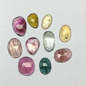 Peut inclure: Une collection de pierres pr&eacute;cieuses facett&eacute;es de diff&eacute;rentes formes et couleurs, dont rose, jaune, vert et transparent. Les pierres pr&eacute;cieuses sont de forme ovale, en goutte et irr&eacute;guli&egrave;re. Les pierres sont expos&eacute;es sur une surface blanche.