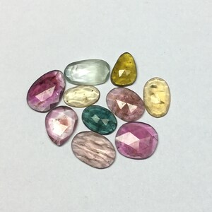 Peut inclure: Une collection de pierres pr&eacute;cieuses facett&eacute;es de diff&eacute;rentes formes et couleurs, dont rose, jaune, vert et transparent. Les pierres sont dispos&eacute;es sur une surface blanche, mettant en valeur leurs diff&eacute;rentes tailles et teintes. Id&eacute;al pour la joaillerie.