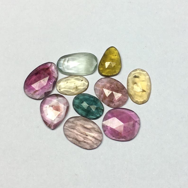 Peut inclure: Une collection de pierres pr&eacute;cieuses facett&eacute;es de diff&eacute;rentes formes et couleurs, dont rose, jaune, vert et transparent. Les pierres sont dispos&eacute;es sur une surface blanche, mettant en valeur leurs diff&eacute;rentes tailles et teintes. Id&eacute;al pour la joaillerie.