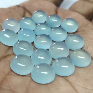 May include: A collection of 18 light blue cabochon gemstones, each with a smooth, rounded surface. The stones are arranged in a loose pile on a hand.