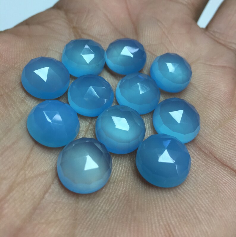 Pu&ograve; includere: Una collezione di dodici cabochon di pietre preziose blu chiaro, ognuno con una forma arrotondata sfaccettata. Le pietre sono disposte in un cerchio sciolto su una mano.