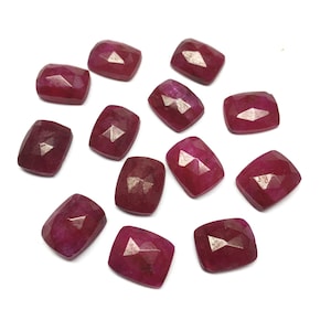 Può includere: Una collezione di 13 pietre preziose di rubino sfaccettate, ciascuna con un colore rosso intenso e una forma a cuscino.