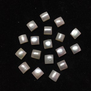 May include: A collection of seventeen small, square-shaped mother-of-pearl buttons. Each button features a smooth, iridescent surface with a soft white sheen that reflects light, showcasing the natural luster and pearlescent quality of the material.