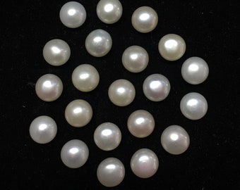 May include: A collection of seventeen loose, round, white pearls arranged in a circular pattern. Each pearl exhibits a smooth, lustrous surface with subtle iridescent highlights, reflecting light to create a bright, polished appearance against the dark background.