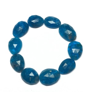 Peut inclure: Une collection de dix pierres précieuses bleues ovales et facettées disposées en cercle. Les pierres ont une couleur bleu profond et vif avec de multiples facettes. Les pierres sont posées sur un fond blanc. Chaque pierre mesure environ 1,5 cm de long.