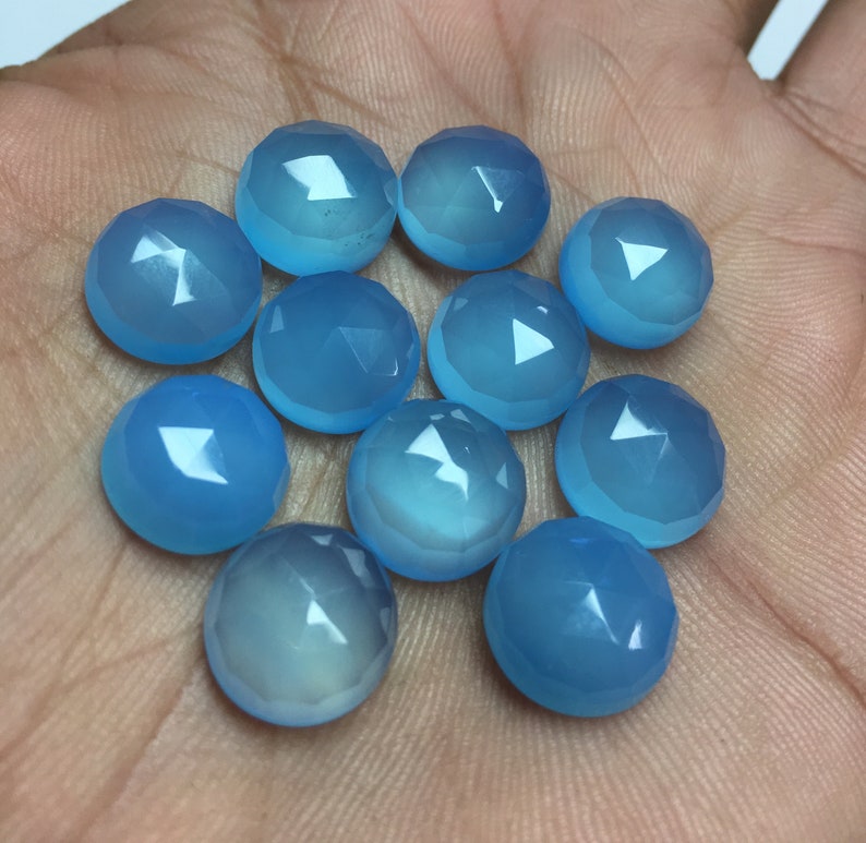 Pu&ograve; includere: Un gruppo di dodici cabochon di pietra preziosa blu chiaro, ognuno con una forma arrotondata sfaccettata. I cabochon sono disposti in un cerchio sciolto su una mano.