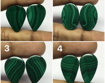 May include: Four pairs of green malachite cabochons, each pair is a different shape. The cabochons are displayed on a hand.