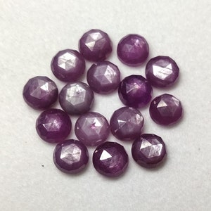 Könnte beinhalten: Eine Sammlung von 15 violetten Sternrubin-Edelsteinen, jeder mit einer facettierten, runden Form.