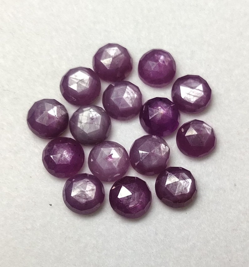 K&ouml;nnte beinhalten: Eine Sammlung von 15 violetten Sternrubin-Edelsteinen, jeder mit einer facettierten, runden Form.