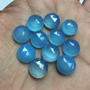 Pu&ograve; includere: Una collezione di dodici cabochon di pietre preziose blu chiaro, ognuno con una forma arrotondata sfaccettata. I cabochon sono disposti in un cerchio sciolto su una mano.
