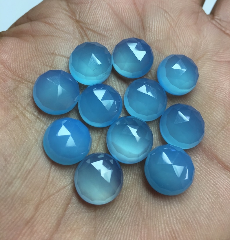 Pu&ograve; includere: Una collezione di dodici cabochon di pietre preziose blu chiaro, ognuno con una forma arrotondata sfaccettata. I cabochon sono disposti in un cerchio sciolto su una mano.
