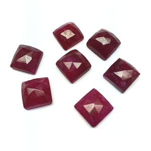 Puede incluir: Siete cabujones de piedra preciosa de color rojo rubí facetados, cada uno con forma cuadrada, están dispuestos en forma de estrella sobre un fondo blanco.