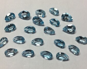 May include: A collection of 19 pear-shaped, light blue gemstones. The gemstones are arranged in a loose, scattered pattern on a white surface.