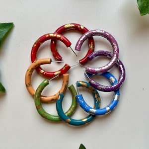 May include: A set of six colourful hoop earrings with gold flecks. The hoops are in shades of red, orange, yellow, green, blue, and purple.