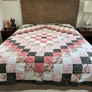 May include: A patchwork quilt featuring a repeating square pattern in shades of dusty rose, dark forest green, and cream. The design incorporates alternating blocks of solid rose, striped fabric, and floral prints arranged in a geometric grid.